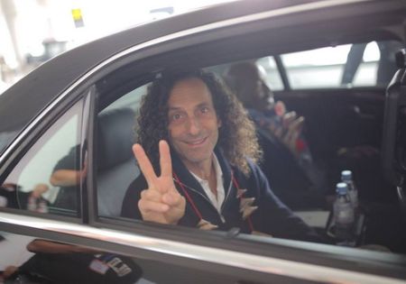 Kenny G in a black suit poses in his car.